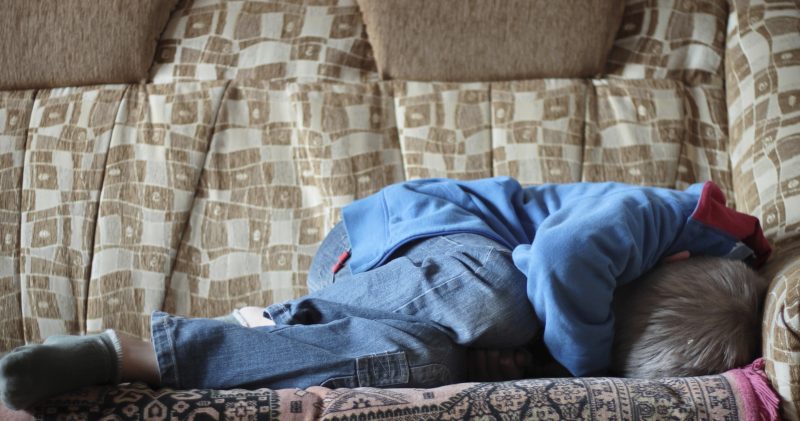 Frightened boy in jeans curled up on bed | Komarovskyy Mykola