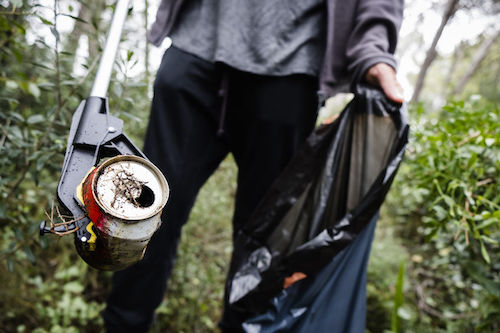 closeup of a caucasian man collecting garbage with a trash grabber stick, in a forest, as an action to clean the natural environment