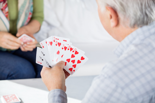 Cropped image of senior man playing cards with female friend at nursing home
