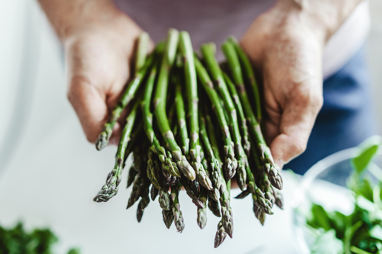 Clean eating or vegetarian concept. Young man holding fresh bundle of asparagus in the kitchen. Closeup.